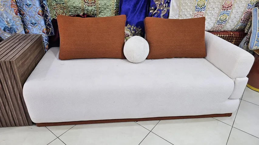 كنبة عصرية بيضاء بوسادتين بلون الصدأ ووسادة دائرية